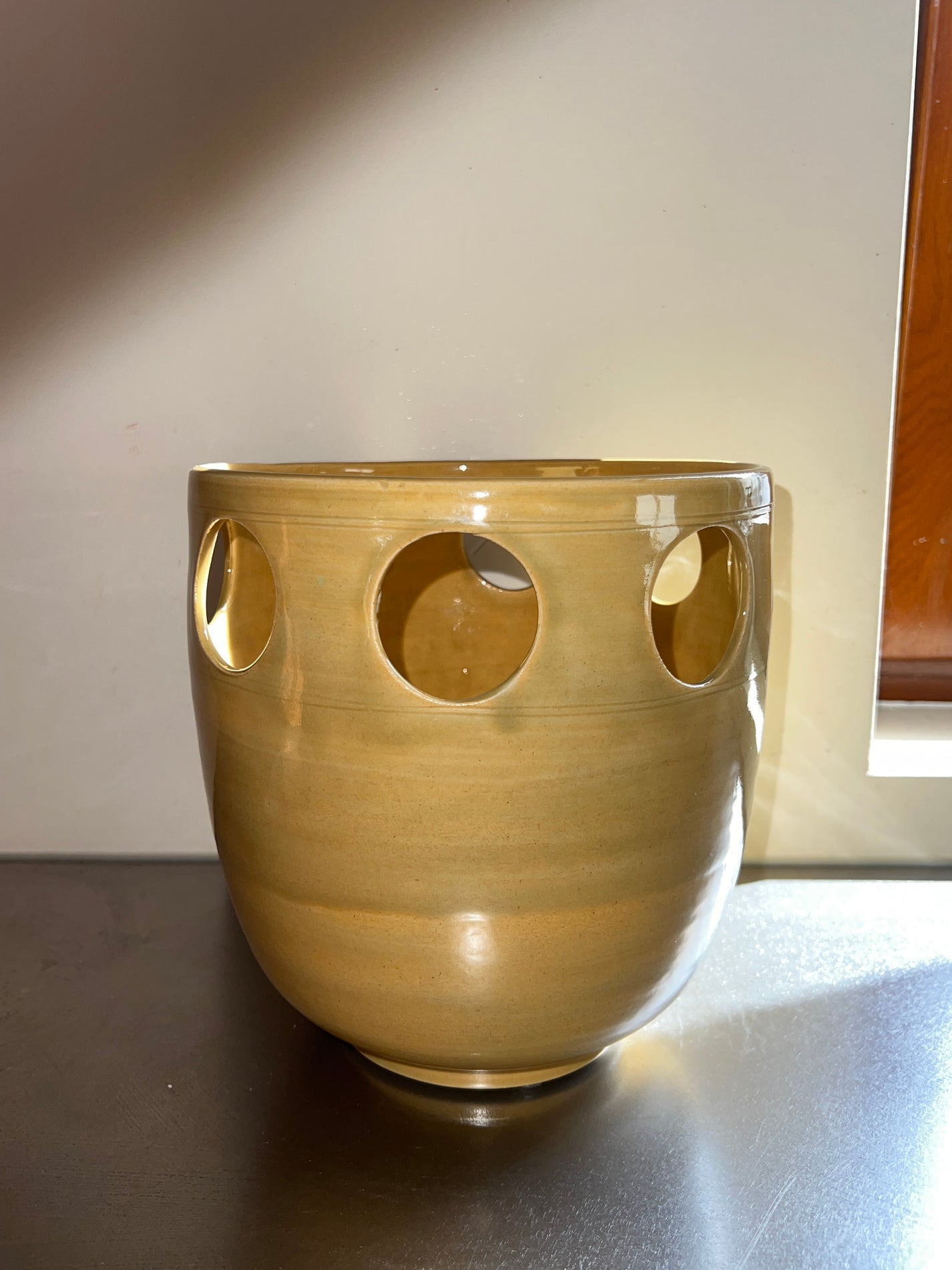 Ajouré Vase #1 in Goldgreen with a band of circular cut-outs, on a dark table in daylight